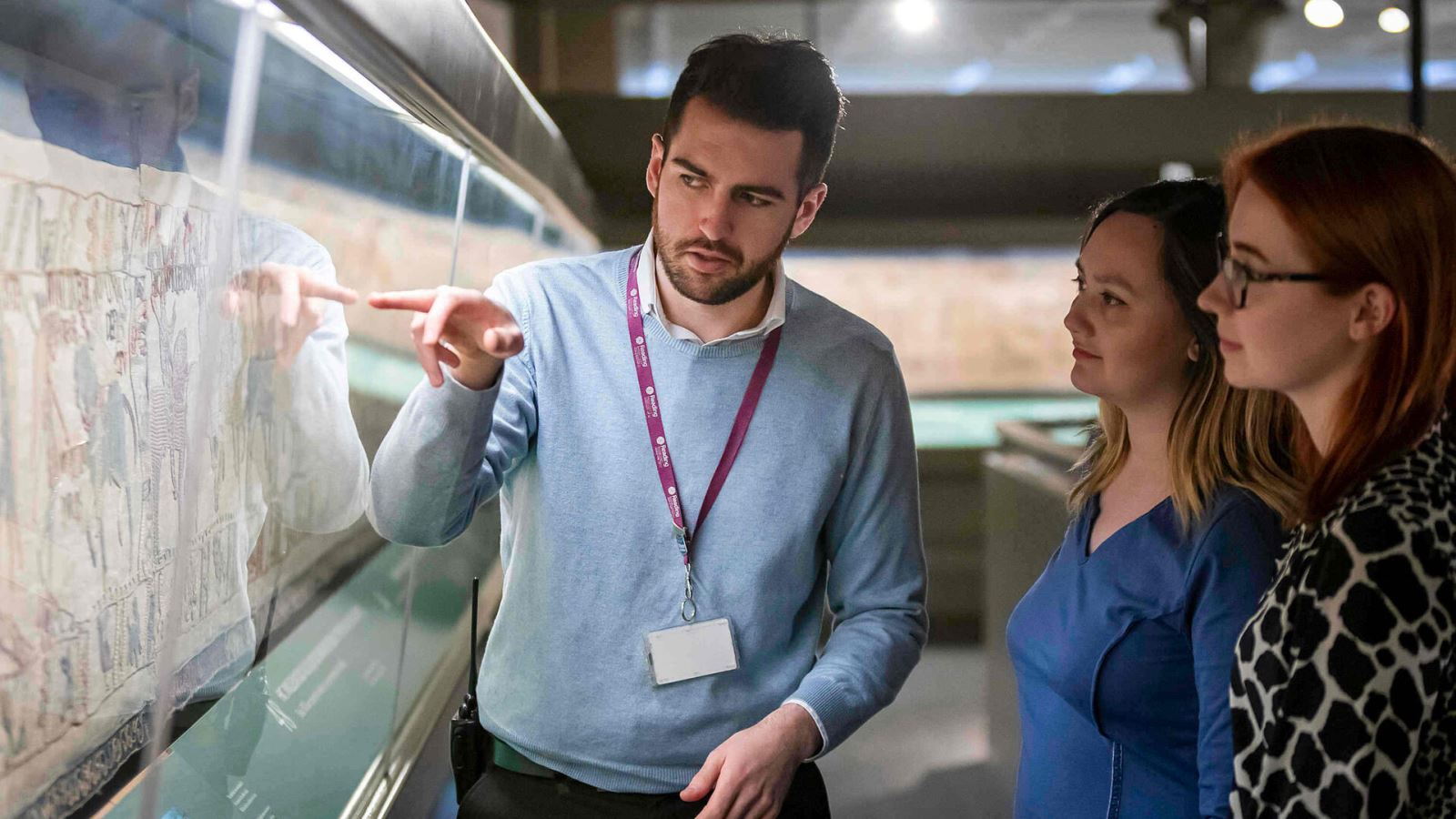 Museum staff showing two visitors Britain's Bayeux Tapestry